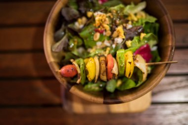 Grilled vegetables and healthy salad of fresh tomato, peanut, cucumber, onion, lettuce and sesame by top view on wooden bowl