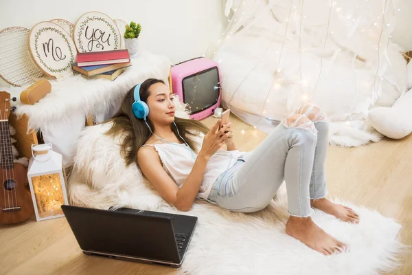 Attractive beautiful Asian woman play social media, shopping online,  listen music video by smartphone and earphone in fancy living room.
