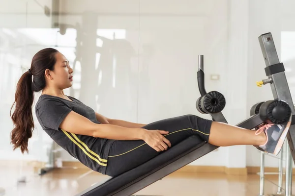 Active slim young Asian Chinese woman doing sit up exercise with machine at fitness gym. Sport and healthy concept with copys space for text.