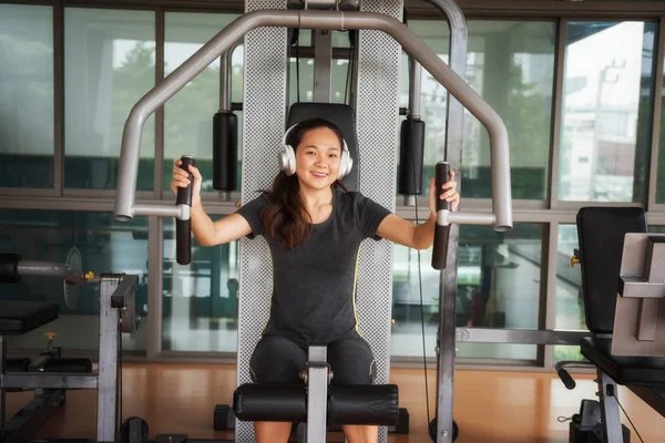 Güzel genç Asyalı kadın egzersiz egzersiz jimnastik salonu makinedeki uygun. Memnun gülümseyen kız onu eğitim süreci ile keyfini çıkarın. Fitness, sağlıklı, spor, yaşam kavramı