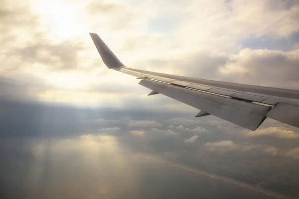 Vleugel van vliegtuig met stralen door wolken — Stockfoto