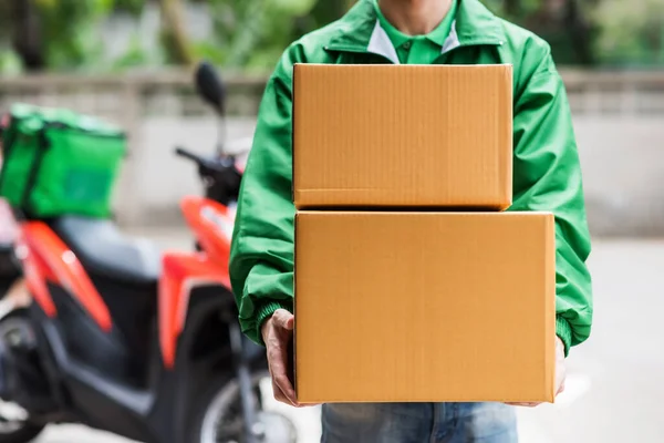 Home delivery parcel boxes by deliver man with green jacket uniform with blur motorcycle background. Online shopping by mobile application. House courier and deliver service mind concept. New normal