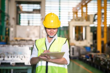 Fabrika teknisyeni ünlü müfettişi arkaplanda bulanık depo mekanizması geçmişine sahip dahili inceleme için denetim raporu yazıyor. Güvenlik iş süreci için kalite güvencesi (QA).