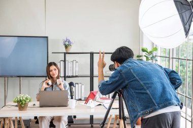 Video ya da profesyonel dijital kameraman stüdyo ışıklandırmalı güzel Asyalı kadın blogger podcaster 'ının canlı yayınını çeker ya da kaydeder. çevrimiçi günlük veya web sitesi içeriği için yayın.