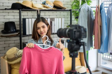 Canlı yayın içeriği üç ayaklı dijital kamerayla çevrimiçi moda satmak için. Güzellik blogcusu ya da internet etkileyicisi. Genç Asyalı kadın vlogger blogları sosyal medyada pembe gömlek gösteriyor.