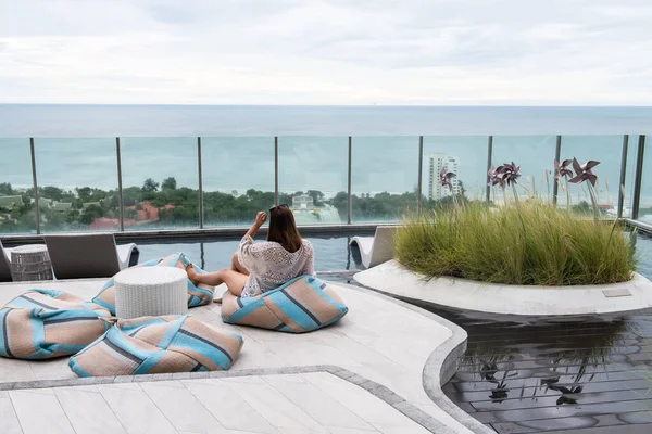 年轻的亚洲女人坐在柔软的豆袋上 在酒店游泳池的屋顶上放松地观赏都市风景和海滨风景 华欣夏季豪华旅游或度假 — 图库照片