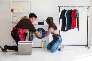 Önlük ve eldivenli neşeli Asyalı çift hafta sonları evde çamaşır yıkıyor. Ev işlerinde çalışan mutlu eş ve koca..