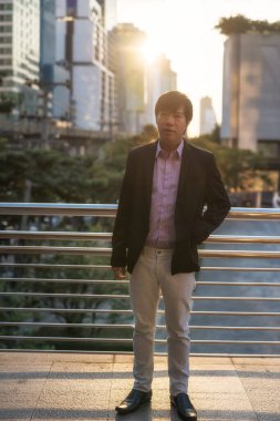 Günbatımında modern şehirde kentsel yapı geçmişi olan yakışıklı Asyalı orta yaşlı iş adamı portresi. Sıradan üniformalı bir işçinin portresi.