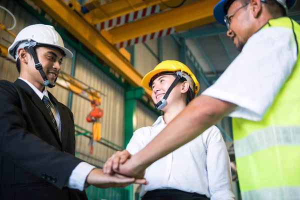 Factory industrial teamwork. Working team stack hands together of businessman, female engineer specialist, and old worker with safety hardhat helmet. Synergy and happyiness concept