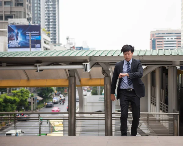 Endişeli Asyalı iş adamı koşuyor ve yoğun saatlerde şehir yürüyüş merdivenlerini kontrol etmek için saate bakıyor. Genç adam tren yolculuğuna, işe, toplantıya geç kaldı. Ofis hayatı ve iş rekabeti.