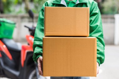 Bulanık motosiklet geçmişi olan yeşil ceketli kurye teslimatçısıyla eve paket kutuları. Mobil uygulamayla online alışveriş. Ev servis konsepti. Yeni normal covid19.