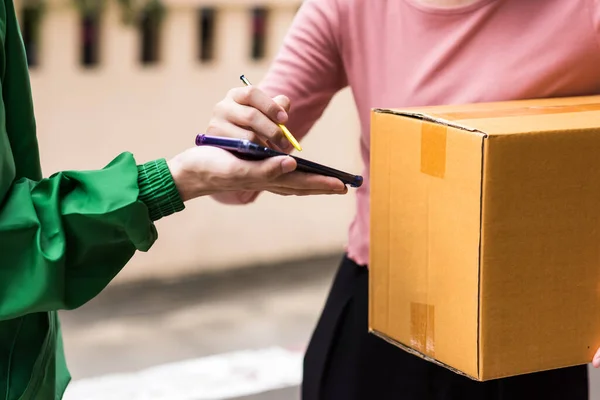 hand of asian woman appending signature sign on smartphone after accepting receive boxes from delivery man in uniform. New normal delivery business during covid19 pandemic. Shopping online.