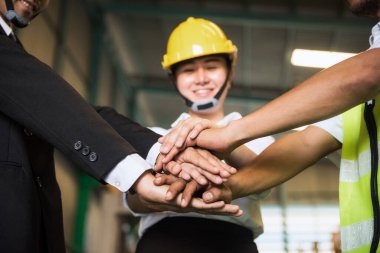 Fabrikada gülen surat ifadesiyle mutlu bir takım çalışması. Depo sahibi, yönetici, kadın uzman ve fabrikadaki eski ustabaşı el ele tutuşsun. Sinerji ve başarı kavramı.