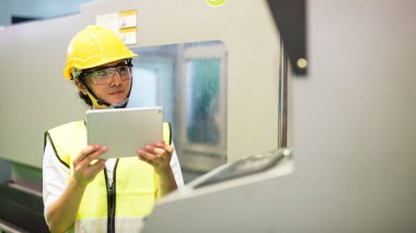 Kask ve koruyucu gözlük takan kadın mühendis CNC 'yi bilgisayar tabletinden G-Code programlama yüklemesi ile donattı. Üretim endüstrisi ve teknoloji.