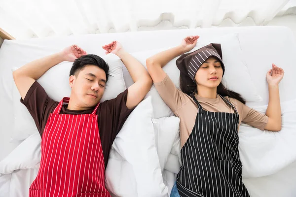 Tired couple with apron sleep or nap on bed by top view after cleaning home at bedroom. Housework on weekend of young exausted Asian husband and wife. End of house cleaning