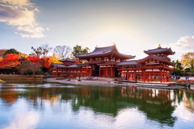 Renkli sonbahar akçaağaç yaprakları ve günbatımında ufuk çizgisi yansıması olan Phoenix Byodo-In Tapınağı, Uji, Kyoto, Japonya. Aralık ayında Kansai 'de turistler için ünlü bir tatil beldesi..