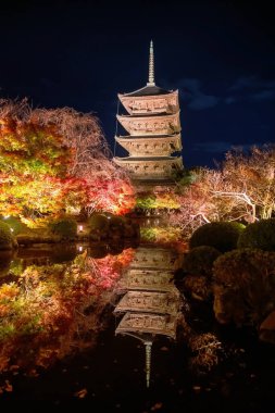 Beş katlı Toji Pagoda 'nın dikey görüntüsü ve sonbahar bahçesi gece ufuk çizgisi yansıması ile gölün kenarında parlıyor, Kyoto, Japonya. Turist gezisi için Kansai 'yi sonbahar aydınlanması için gezme yeri