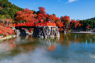 Japonya, Minoh, Osaka 'daki Katsuo-ji Tapınağı' nda mavi gökyüzüne karşı buharlı ve sonbahar yaprak bahçeli gölet tapınağa Torii kapısı. Sonbaharda Kansai 'yi görmek için ünlü bir seyahat yeri. Zafer tapınağı