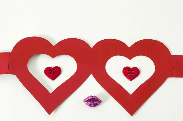 Cute face made from heart shape glasses, little red heart shape buttons and little purple lips against white background