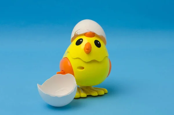 Cute yellow toy chicken with cracked egg against blue background
