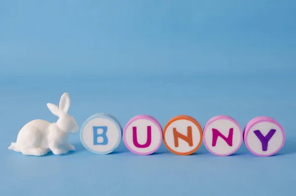 Bunny word made from colorful letters and white bunny on blue background. Easter decoration