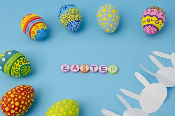 Colorful decorated eggs, white bunny paper chain and Easter made from colorful letters on blue background. Easter Day decoration