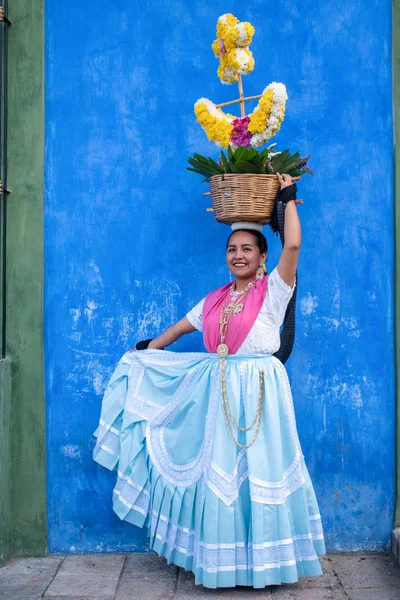 Oaxaca, Oaxaca, Meksika- Temmuz 6, 2019: Genç kadın Convite sırasında renkli çiçeklerle süslenmiş bir sepet taşıyan geleneksel giysiler ile giyinmiş, oaxaca Guelaguetza adlı büyük bir geleneksel partiye davet için yapılan bir parti, Meksika
