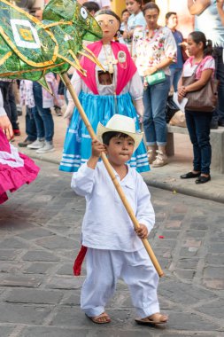 Oaxaca, Oaxaca, Meksika- Temmuz 6, 2019: Convite sırasında selofan yapılmış yeşil bir çekirge taşıyan küçük çocuk, Oaxaca Guelaguetza adlı büyük bir geleneksel partiye davet için yapılan bir parti, Meksika