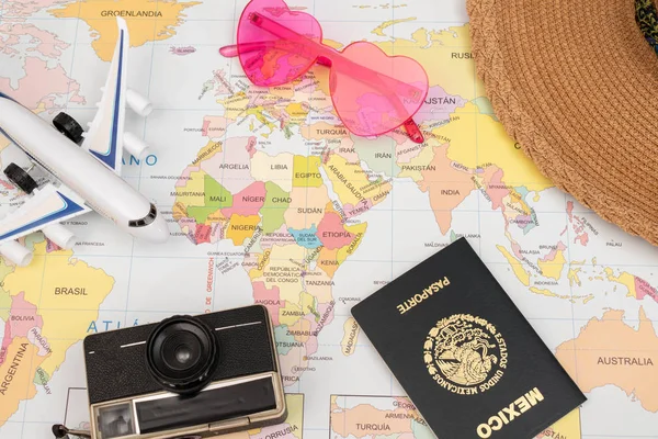 Vintage camera, pink sunglasses, passport, hat and compass on a map as background