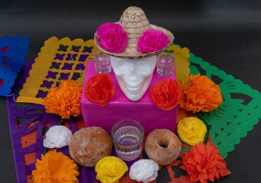 Geleneksel ekmek, renkli çiçekler, beyaz kafatası ve siyah arka planda kesilmiş kağıt içeren Meksika Ölüler Günü.