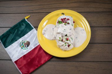 Tipik Meksika yemeği, sarı tabakta Chiles en nogada ve tahta arka planda Meksika bayrağı.