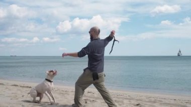 Genç adam sahilde köpeğiyle oynuyor.