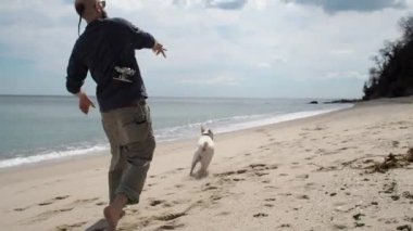 Genç adam sahilde köpeğiyle oynuyor. Arkadan vurdu