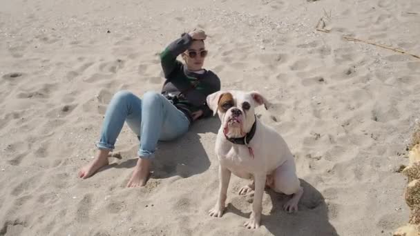 Slow motion di un carino caucasico donna e il suo bianco boxer cane relax sulla spiaggia — Video Stock