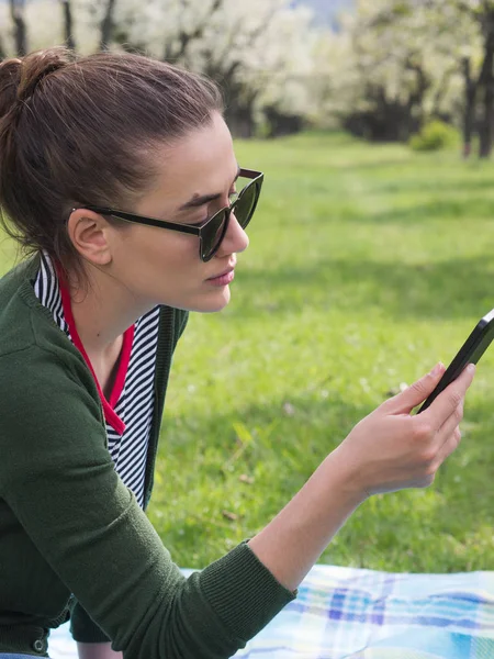 Портрет молодой красивой женщины, которая пишет смс на смартфоне, расслабляясь на открытом воздухе — стоковое фото