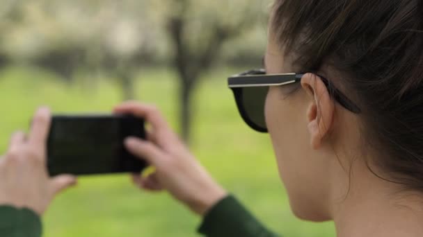 Vista trasera de una joven mujer caucásica en la naturaleza tomando fotos con su teléfono inteligente — Vídeo de stock