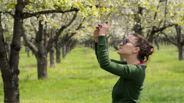 Вид сбоку на молодую кавказскую женщину в природе, фотографирующую со своим смартфоном — стоковое видео