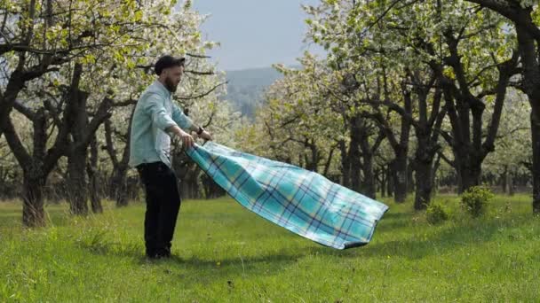 Egy fiatal férfi hozza egy takarót a füvön, a parkban egy romantikus vacsorára egy barátnője — Stock videók