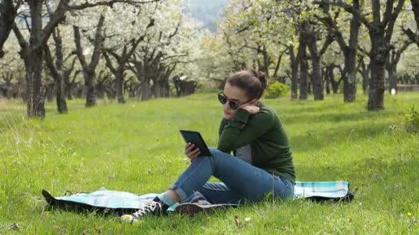 Щаслива жінка читає електронну книгу в парку — стокове відео
