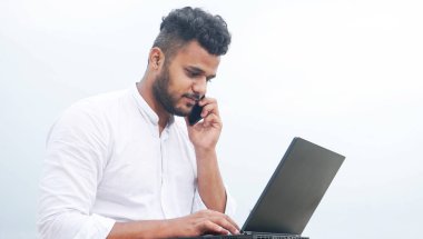 Genç adam dizüstü bilgisayar ve akıllı telefonu birlikte kullanıyor.