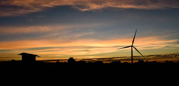 Silhouette wind turbines and cottage at sunset — Stock Photo, Image