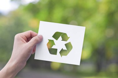 Çevre konsepti. Yeşil bokeh arkaplan üzerinde geri dönüşüm sembolü olan beyaz kağıt tutarken.