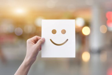 El ele tutuşan gülen surat ifadeli beyaz kağıt (delikli kağıt) arka planda hafif bokeh.