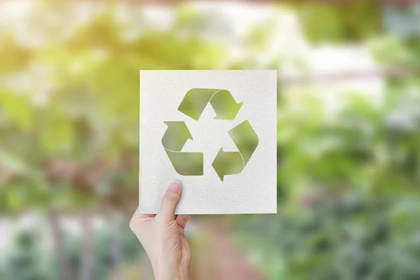 Kesik kağıt ile logo geri dönüşümü ile el ele tutuşmak bulanık yeşil doğa arka planı.