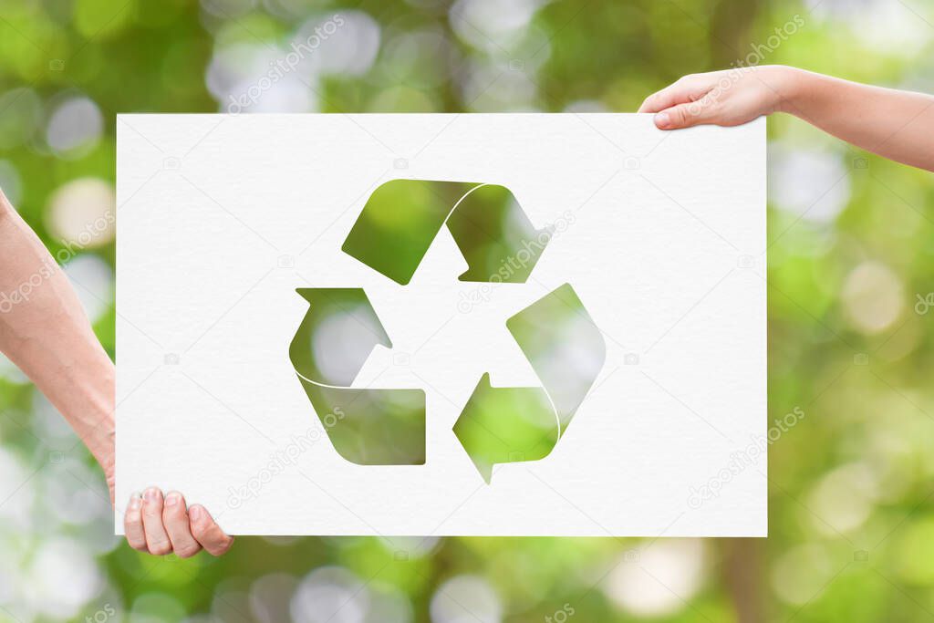 Hand holding white board with recycle logo over green nature background. Earth day concept