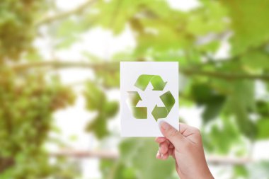 Yeşil doğa arka planında geri dönüşüm logosu olan beyaz kart tutan bir çocuk. Dünya Günü konsepti