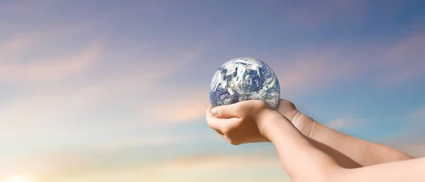 environment day concept, Globe in child hands over blue sky background. save of earth. Elements of this image furnished by NASA