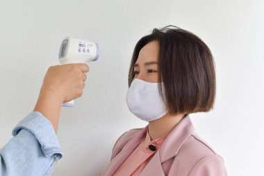 Vücut ısısını ölçmek için el ele tutuşan kızılötesi alın termometresi. Coronavirus 'tan koruma kavramı (COVID-19). Salgın - Sağlık Hizmetleri