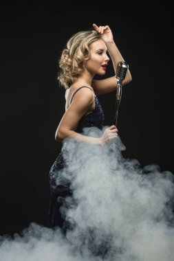 Sexy genç kız şarkıcı sahne duman siyah zemin üzerine gümüş retro mikrofon ile şarkı