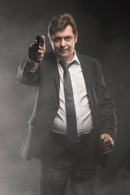 Orta yaşlı dedektif yakışıklı koyu arka plan üzerinde silahla